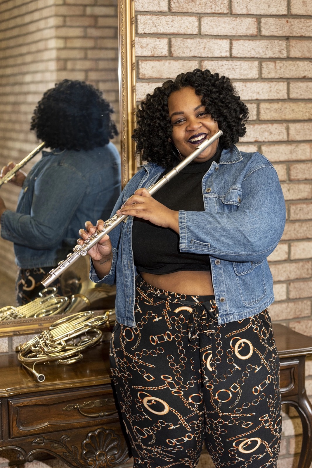 Shanyse Strickland playing flute beside a mirror reflecting her horns